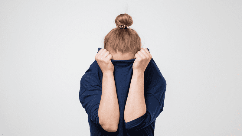 European woman hiding her face in her shirt in front of white background