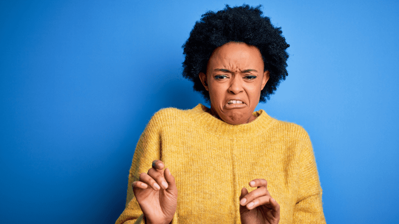 Black woman in a yellow sweater with an disgusted expression standing in front of a bright blue background