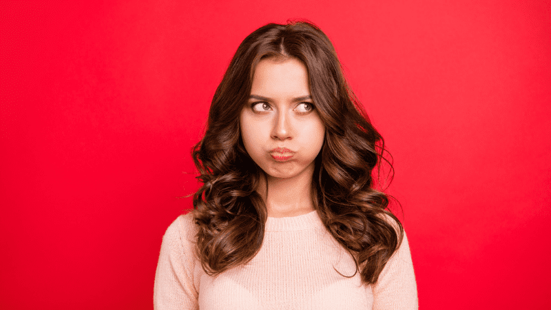 White woman blowing out her cheeks in frustration in front of a bright red background