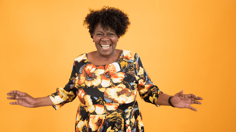 Overjoyed Black woman in a patterned dress in front of a bright yellow background