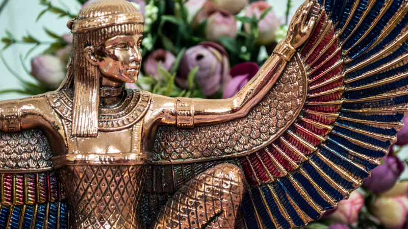 Golden statue of the Egyptian goddess Isis with a bouquet of flowers in the background