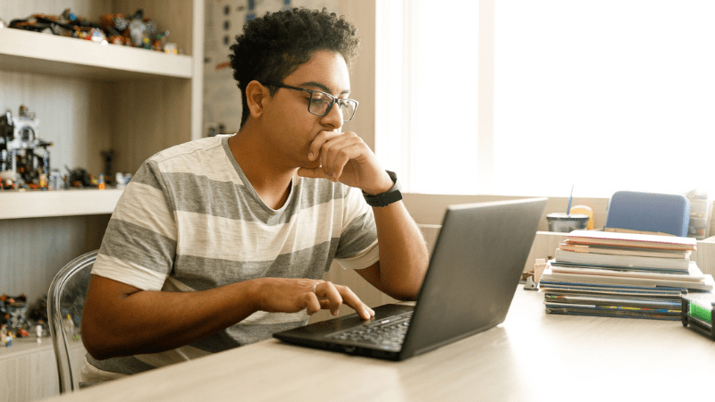 Young male student sitting in front of a laptop at home