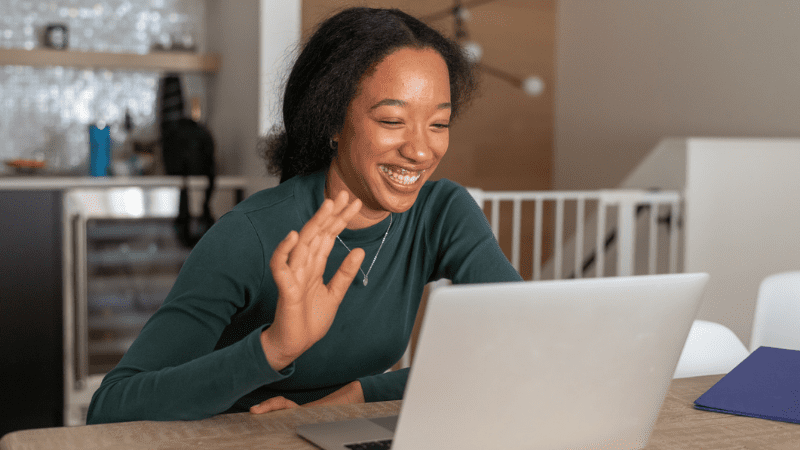 Young Black woman waving at laptop screen