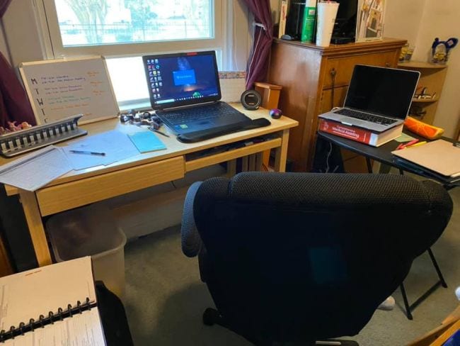 Two laptops set up on desks with plush black computer chair with window in background