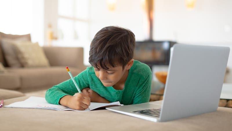 A young boy using laptop while drawing a sketch on book at home.