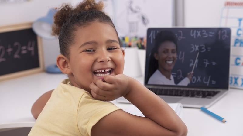 6 years old girl learning at home online, using a laptop computer with a video chat app as her teacher is teaching her multiplication.