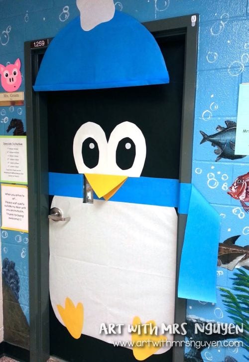 Classroom door decorated as a large paper penguin wearing a blue hat and scarf (Winter Classroom Doors)