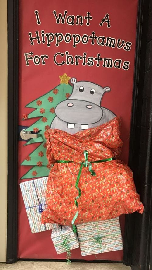 Classroom door decorated with a hippo in a large bag by a Christmas tree. Text reads "I want a hippopotamus for Christmas."