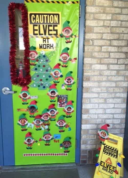 Classroom door decorated with paper elves with photos of student faces. Text reads "Caution: Elves at Work"