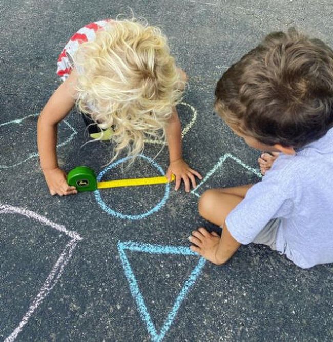 Students using a measuring tape to measure shapes drawn on the ground with sidewalk chalk