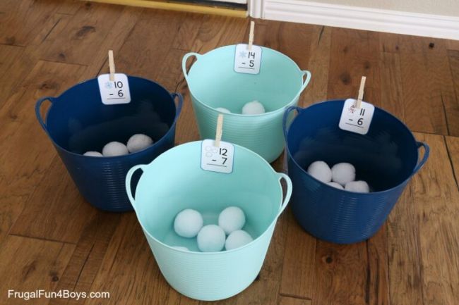 Four plastic buckets with math flashcards clothespinned to them, with large white pom poms in each (Active Math Games)