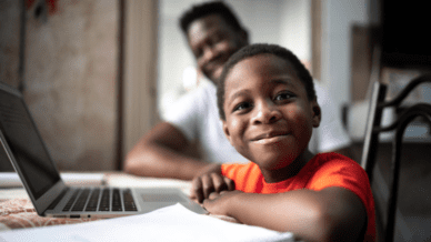 African American boy and his father studying on a laptop when instructors is teaching reading remotely