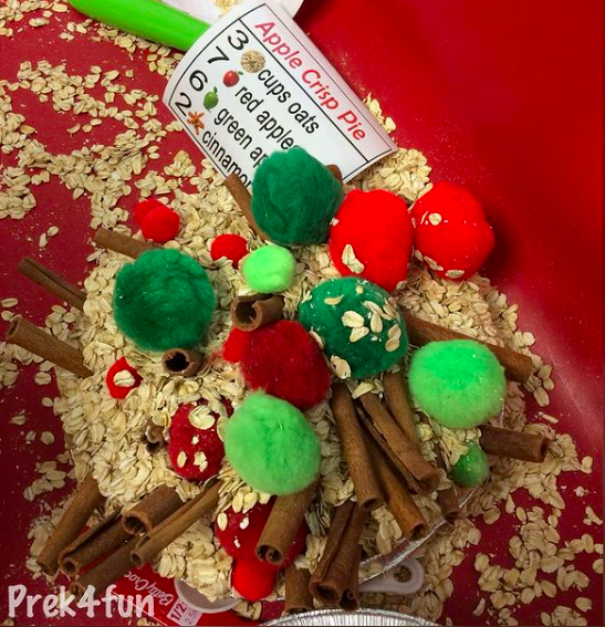 Sensory table with oats, pompoms, cinnamon sticks and recipe card to make pretend apple pie