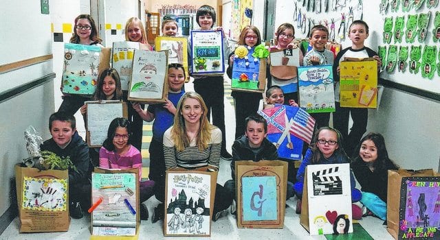 smiling children and their teacher posing with their paper bag book reports