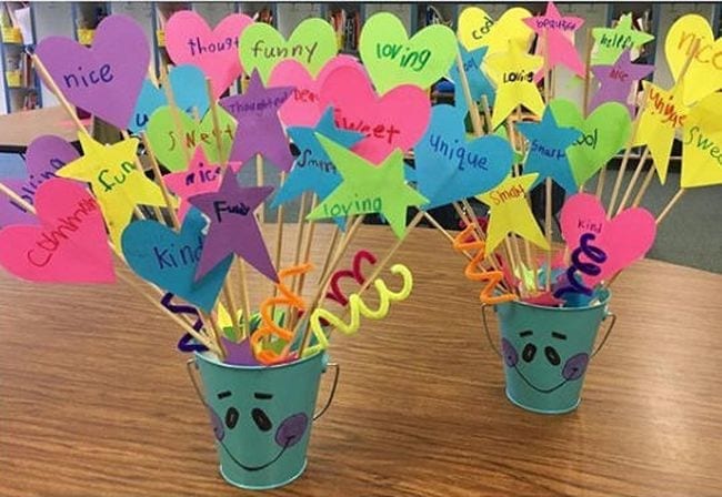 colorful buckets on a classroom desk filled with compliments made from sticks and colored paper