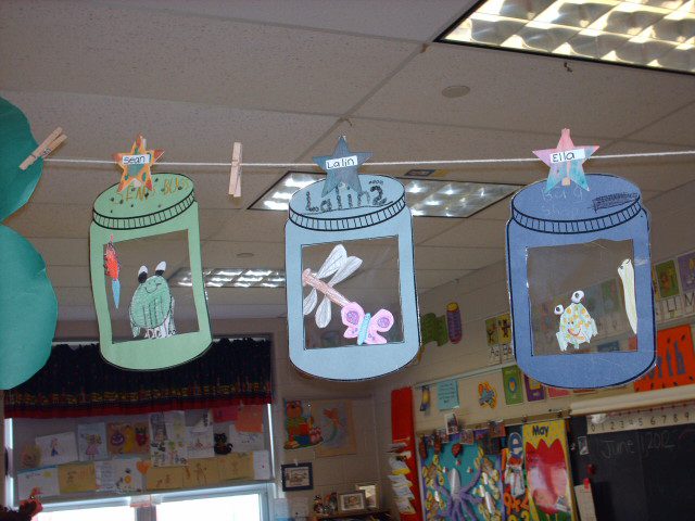 Posterboard cutouts of lanterns are shown with different student drawn creatures in them. They are hanging from clothespins on a clothesline in a classroom.
