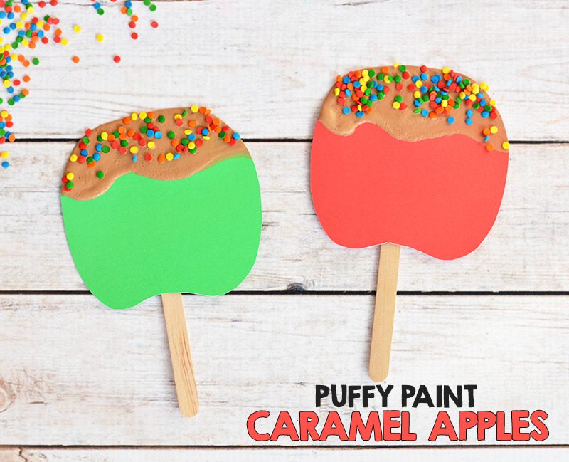 A red and a green candy apple are shown. They are made from posterboard and a popsicle stick. Brown puffy paint is on the top to look like caramel and sprinkles are on it.