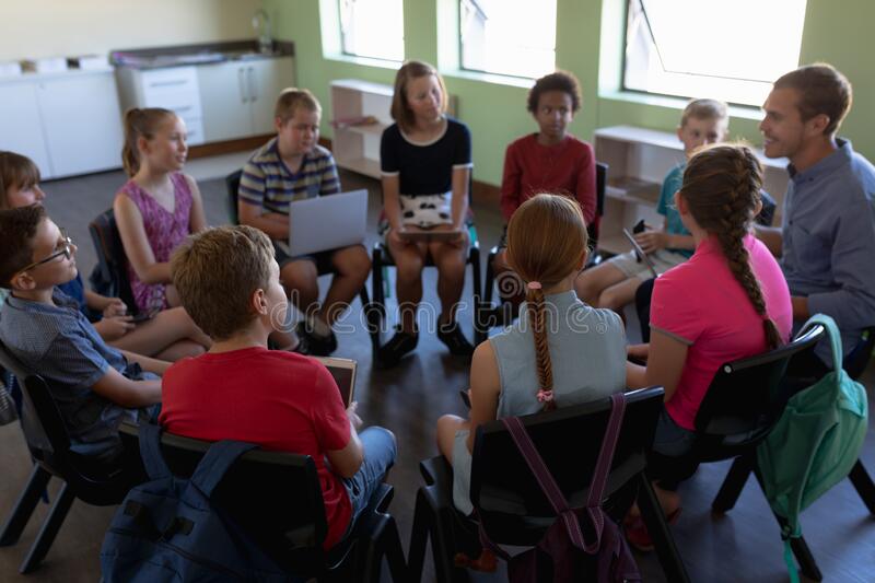 elementary aged kids and teacher sitting in chairs in a circle