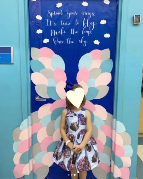 Classroom door with butterfly wings and child standing in front. Text reads Spread your wings, it's time to fly. Make the leap, own the sky.