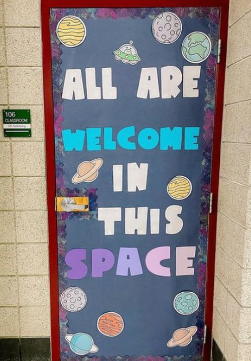Classroom door decorated with pictures of planets and text reading All are welcome in this space