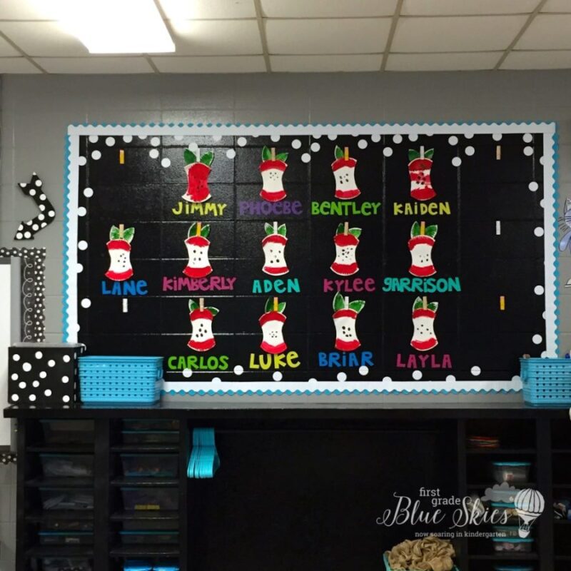 A black September bulletin board has 13 construction paper apple cores hanging from clothespins. Names are under each core in brightly colored letters.