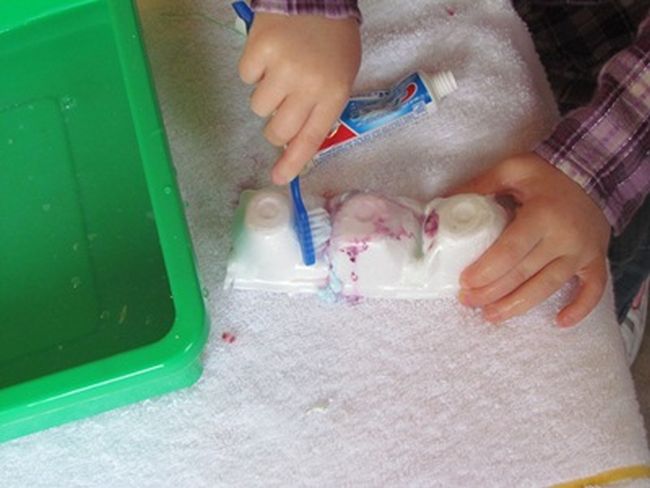 Preschooler using a toothbrush to clean teeth made from an egg carton (Dental Activities for Preschoolers)