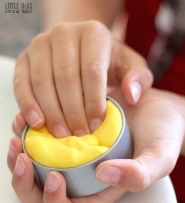 Child playing with a tin of yellow putty