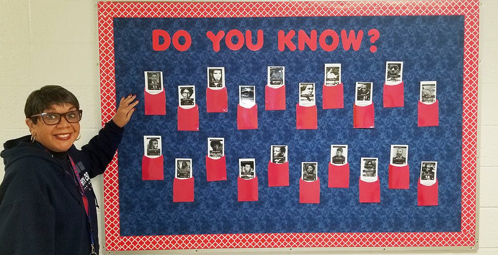 A woman standing in front of a bulletin board that says Do you know?  across the top.  It has photos of famous black people on it with flaps to lift (black history month bulletin board)