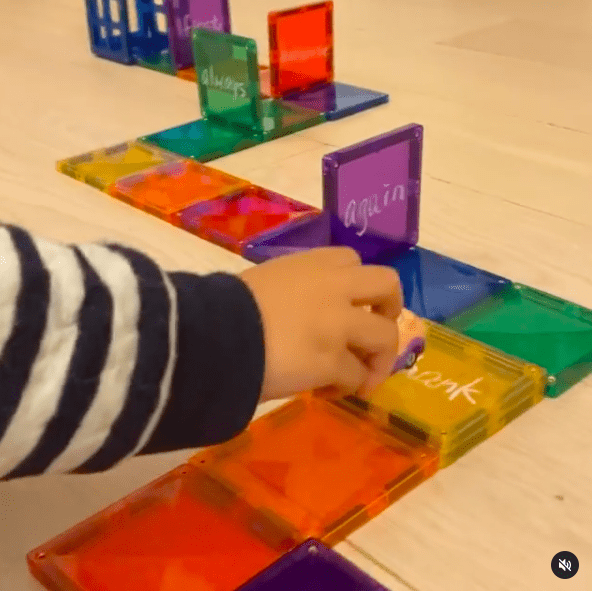 Kinderhand fährt mit einem Spielzeugauto über einen Pfad aus magnetischen Kacheln mit darauf geschriebenen Sichtwörtern's hand driving a toy car over a path of magnetic tiles with sight words written on them