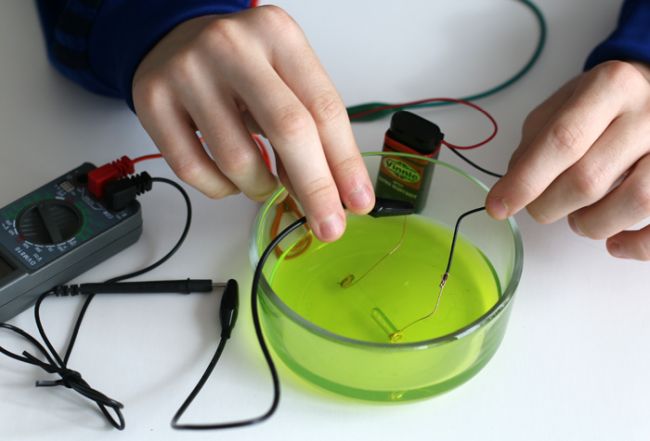 Student using wires to test for electrolytes in a green drink (Eighth Grade Science)