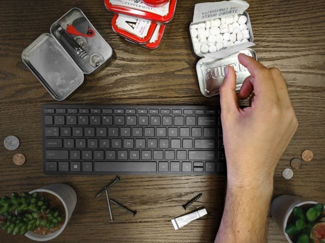 Hand taking an Altoid mint from a tin, with a keyboard and other small items (Eighth Grade Science)