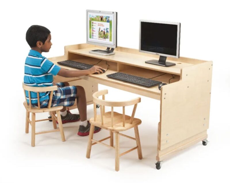 Elementary school boy sitting at wooden computer table in a classroom