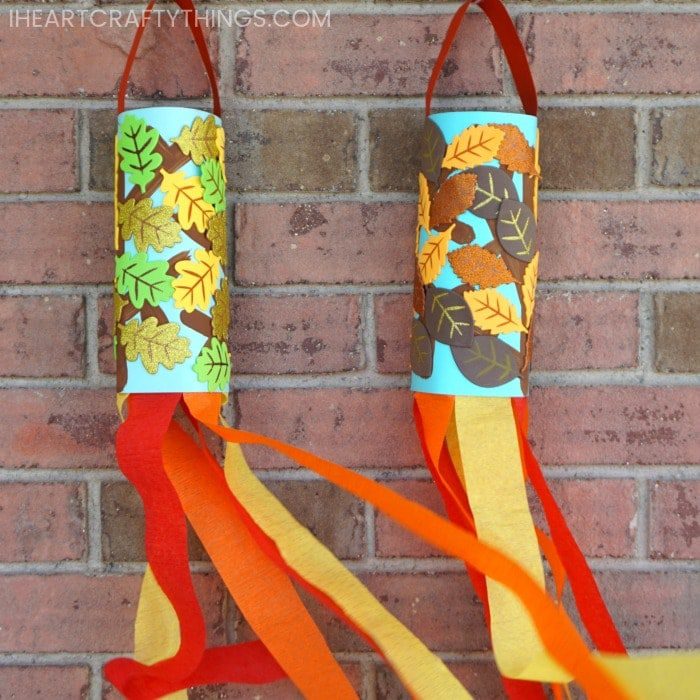 Paper towel rolls are decorated with fall leaves and have handles to hang them from attached. Red, orange, and yellow crepe paper hang from the bottom.