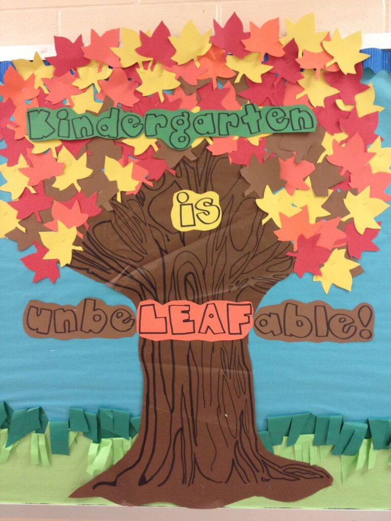 An example of September bulletin board ideas features a large tree with many orange, red, and yellow leaves. "Kindergarten is unbeleafable!" is shown across the tree in green, yellow, brown, and orange writing.