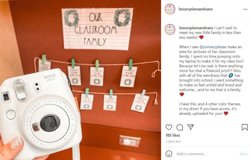 White instant camera in the foreground with a nook that says "Our Classroom Family" behind it with hangers for displaying photos.