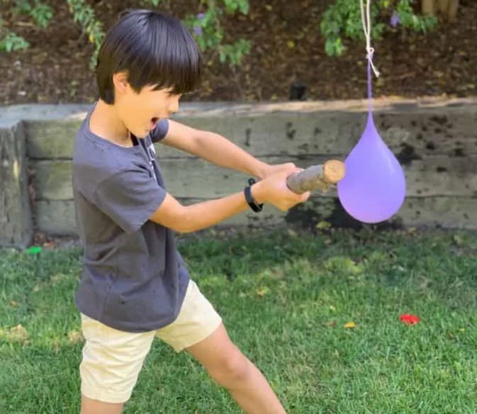 Child using a stick to hit a hanging water balloon (Field Day Games)
