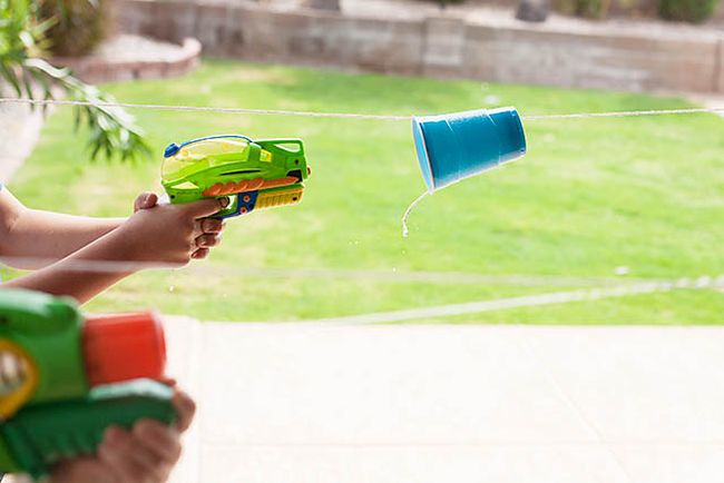 Kid using a squirt gun to propel a plastic cup hung on a string