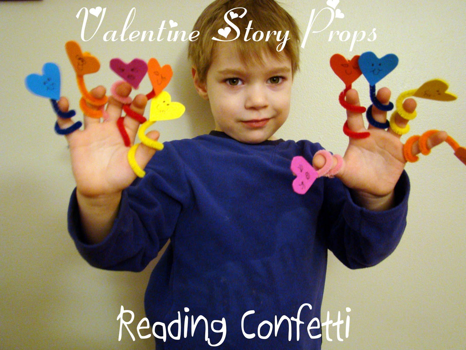 A little boy is shown with "puppets" On his fingers that are made of twisted pipe cleaners and foam hearts with faces drawn on them.