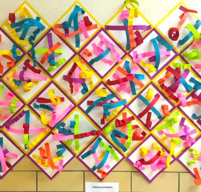 Paper sculptures made of colorful folded paper strips, hung on the wall (First Grade Art)
