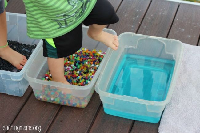 Toddlers walking through plastic tubs filled with different substances