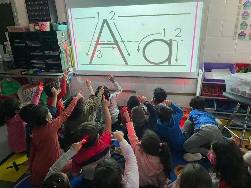 Young students using finger flashlights to trace letters