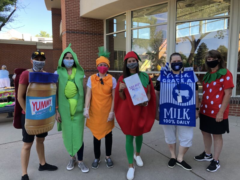 Six teachers are dressed up as different foods including peanut butter, peas, a carrot, an apple, milk, and a strawberry.