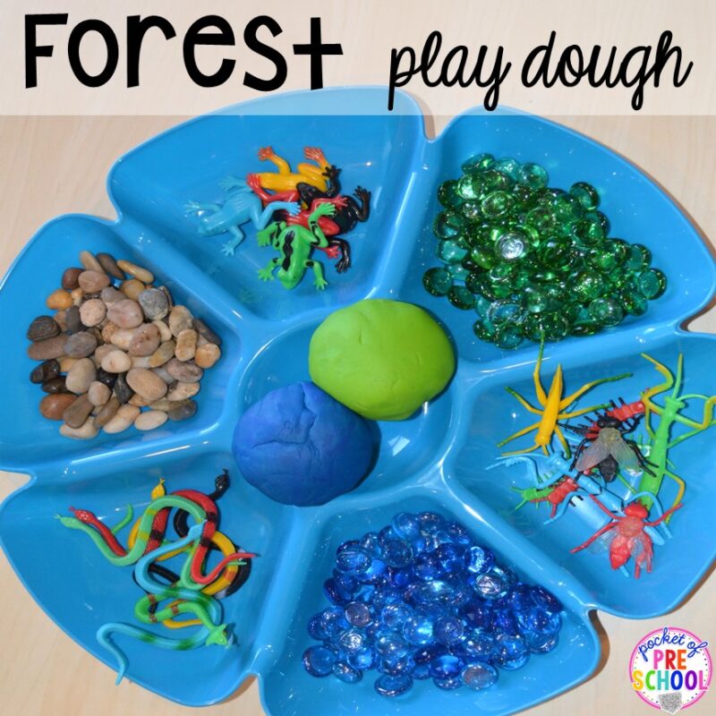 A blue tray with six sections shows a variety of forest themed items including river stones and plastic insects. Blue and green play dough is in the middle. 