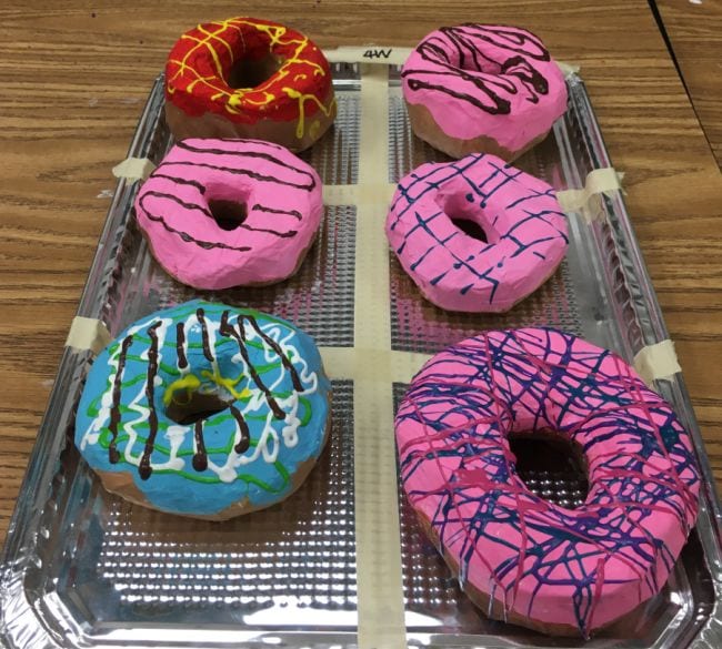 Six colorful donuts made from papier-mâché sitting on a silver tray