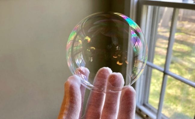 Die behandschuhte Hand des Schülers hält eine Seifenblase neben einem Fenster (Wissenschaft der vierten Klasse)'s gloved hand holding a soap bubble next to a window (Fourth Grade Science)