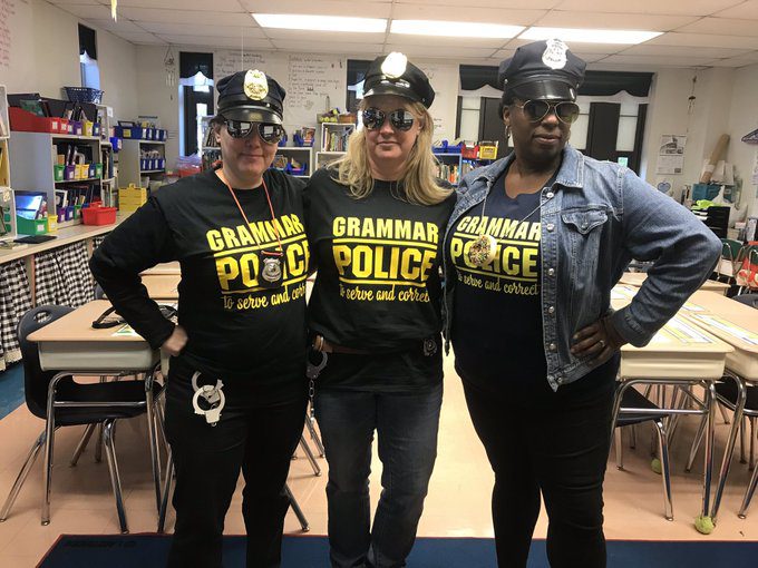 Three teachers are dressed in all black police uniforms. Their shirts read grammar police.