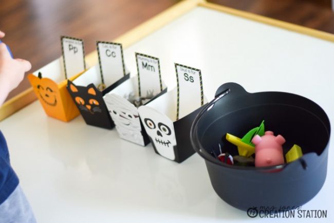 Plastic cauldron holding small toys next to Halloween themed boxes labeled with letters