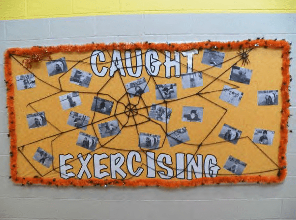 Fall bulletin boards: This one says Caught Exercising and has a spider web all over it. There are photos of students exercising throughout the board.