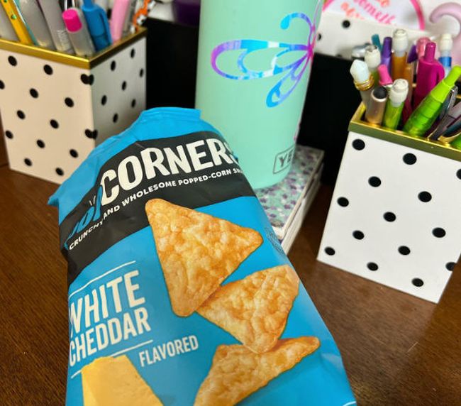 A bag of White Cheddar PopCorners chips with desk supplies