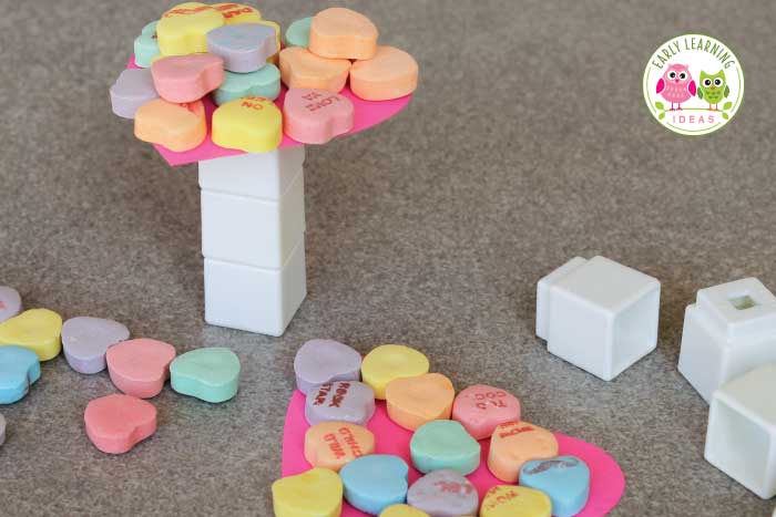 White blocks are shown stacked with a heart on top that has conversation heart candies piled onto it.
